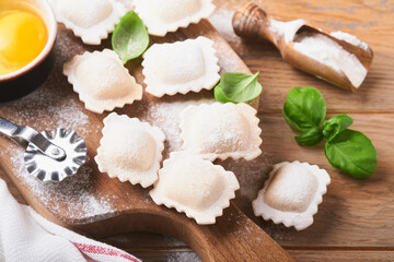 Ravioli Italian food. Tasty homemade pasta ravioli with flour, tomatoes, eggs and greens basil on wooden background. Process of making italian ravioli. Food cooking ingredients background. Top view.