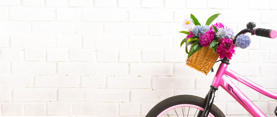 Pink bicycle with a basket of flowers against a brick wall