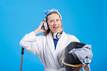 A picture of a young woman in a robe and a headband who is cleaning and listening to music, holding...