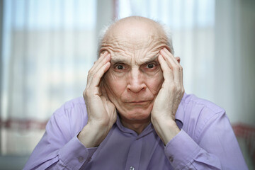 Tired sick man seated at table in room of hospital or house holds temples with hands