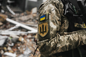 Obraz premium Ukrainian military woman with the Ukrainian flag in her hands on the background of an exploded house