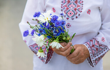 An old Ukrainian woman in an embroidered shirt with a bouquet of flowers. Selective focus.