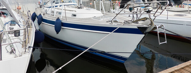 White modern sailboat (for rent and sale) moored to a pier in a yacht marina. Wooden teak deck....