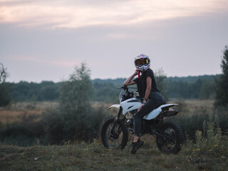 A young slender woman in a helmet on a cross - country motorcycle or pit bike . Moto woman
