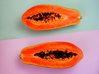 A papaya cut into two halves set against a backdrop of pastel colors, light purple and green. Flat...