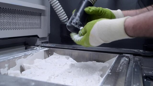 A man working with a working vacuum cleaner to clean the white powder of polyamide from a model printed on a 3D printer inside a 3D printer. Cleaning objects printed on an industrial powder 3D printer