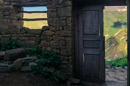 wooden door in the ruins of an abandoned house through which mountains are visible, in the ruins of the ghost village of Gamsutl in Dagestan