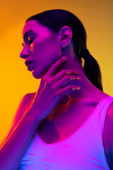Portrait of tender young girl wit nude makeup and low pony rail posing isolated over yellow studio background in neon light