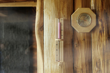 Sand timer and thermometer with hygrometer hanging on the wooden wall of the sauna - obrazy, fototapety, plakaty