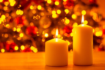 Two burning candles on wooden table on background of decorated christmas tree bright in lights. Christmas celebration, festive atmosphere