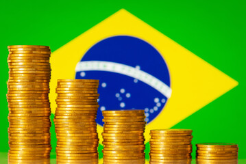 Stacks of coins forming negative graph against flag of Brazil. Concept of economic regression,...