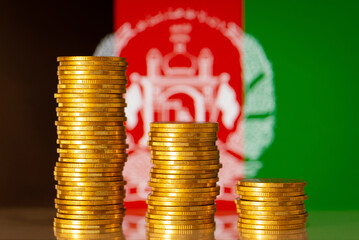 Stacks of gold coins in front of flag of Afghanistan symbolizing crisis in economy of the country....