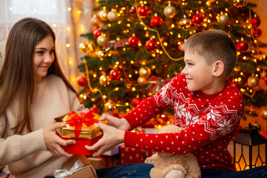 Little Boy And Teenage Girl Siblings Fighting For A Present Sitting Under Decorated Christmas Tree. Christmas Celebration