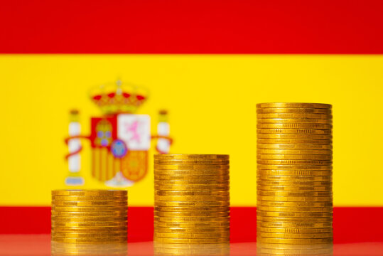 Upgoing graph made of coins stacked in front of Spain flag. Concept of financial development of Spain