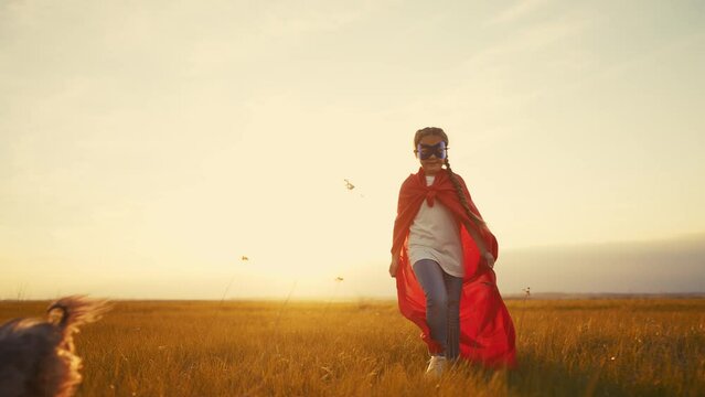 girl superhero. child in a red raincoat runs with a dog outdoors in the park. happy family kid dream concept. little girl superhero runs with a dog across the field lifestyle in nature
