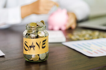 Pile of coins in a bottle on the table and woman picking up a coin for save money, saving money or savings concept.