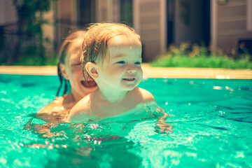 The child has fun outdoors in the pool in the villa. Little beautiful girl is splashing in the pool. The baby is learning to swim. Family happiness