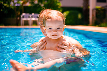 The child has fun outdoors in the pool in the villa. Family happiness. Little beautiful girl is splashing in the pool. The baby is learning to swim