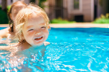 Little beautiful girl is splashing in the pool. The baby is learning to swim. The child has fun outdoors in the pool in the villa. Family happiness