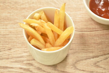 French fries mixed with salt in cup dipping ketchup on table