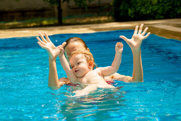 Mom and daughter in the pool. Happy child is having fun. A woman teaches a baby to float on the water and swim. Family happiness. Summer outdoor fun in the pool in the villa