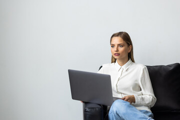 Relaxed woman using laptop in luxury home living room with big window, enjoying working, internet shopping, checking social network with computer sitting on sofa