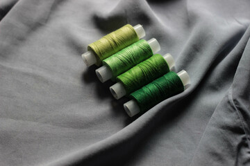 a set of green and light green silk, cotton, synthetic threads in spools against the background of...