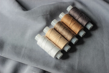 spools of thread in beige, white and yellow hues are laid out in a row on a draped gray fabric