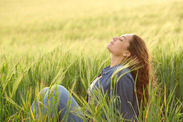 Woman sitting in a wheat field breathing fresh air - 513740722