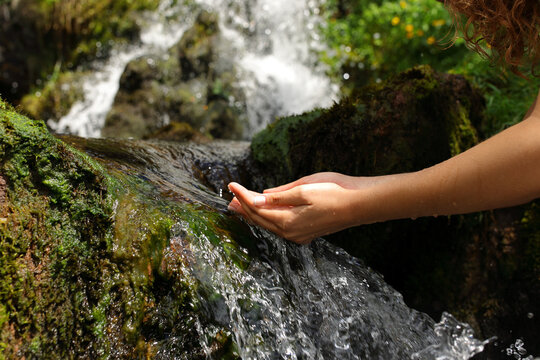 Woman hands cupping catching water from waterfall