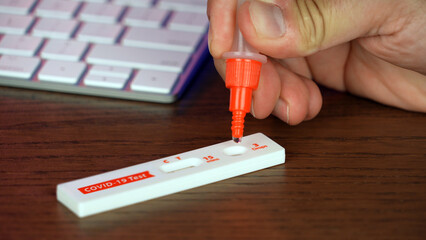 A man performs an at-home COVID-19 test at his desk with a rapid test kit.  	