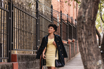 Horizontal image of a very pretty African American woman in a yellow dress walking alone through...