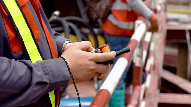 4k, Close Up Hands of an Asian male engineer in a safety suit standing at a construction site operating a machine with a remote control.