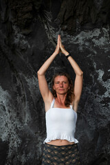 beautiful woman doing yoga against dark rocks vrksasana