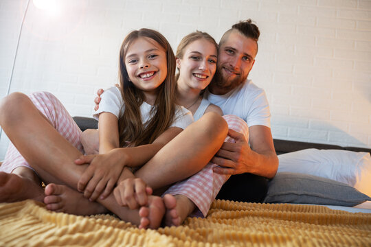 Portrait of parents sitting on bed i bedroom with their daughter.