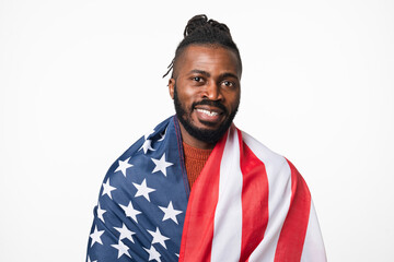 African-american young man covering with American USA flag like patriot looking at camera isolated...