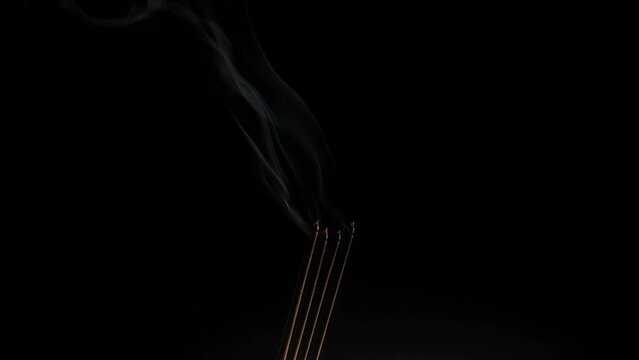 Group of smoldering or burning real red incense sticks coil with thick white smoke isolated on dark black background. Asian indian funeral, prayer, puja, spa and wellness concept. Close up side view.