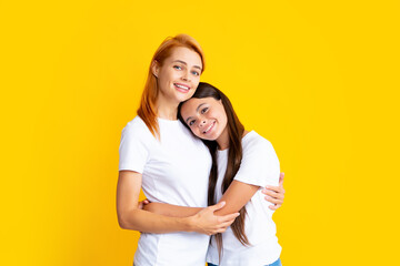 Beautiful mother and daughter smiling happy hugging over isolated yellow background.