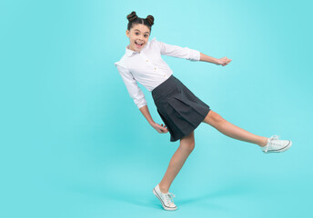 Happy schoolgirl, positive and smiling emotions of teen girl. Full length jump of teenager girl on blue isolated studio wear casual skirt and shirt. Funny school girl, amazed kid genius.