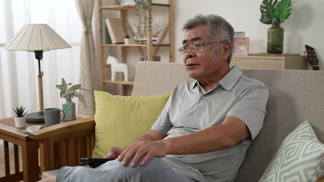 Close up view grey haired grandpa in glasses watching television struggling with news presenter indoors sitting on cozy divan. angry old man nagging with political show on tv