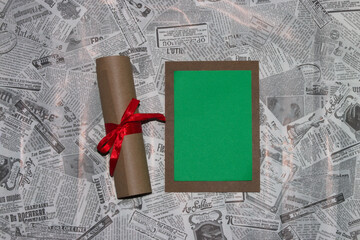 wooden board with green copy space on a newspaper background, next to the board is a scroll with a red bow, creative invitation, greeting card