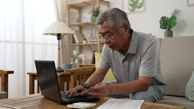 old asian man using laptop and credit card payment shopping online with customer network connection. Older people with technology. senior male using debit card paying internet bargain sale