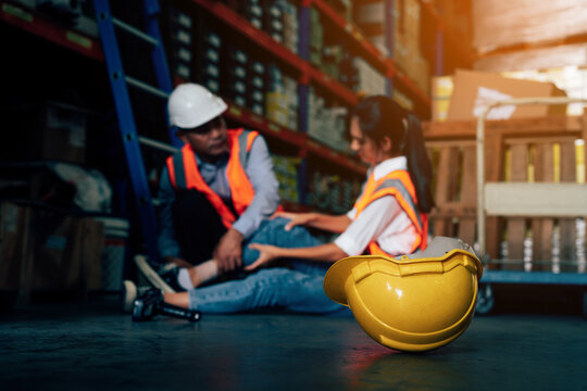 Mature foreman in workwear giving first aid to asian women staff suffering after working injury in warehouse, Injury at work. 