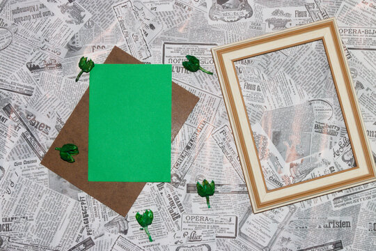 wooden board with green paper as copy space, next to green dried flowers and wooden frame as copy space on newspaper background, creative background, invitation, greeting card