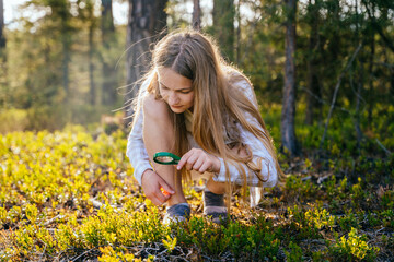 Teenage girl holding magnifying glass explores nature and the environment. Future profession ecologist or biologist. - obrazy, fototapety, plakaty