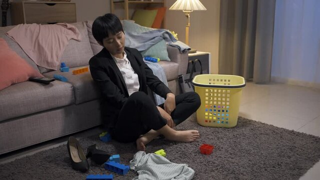 Unhappy Asian Career Mom Is Crossing Her Legs And Looking Into Space With A Sigh Feeling Tired Of Cleaning Up Messy Home Living Room Interior After Work At Night