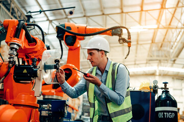 Male engineer checking and inspection control a robot arm machine welding steel in an industrial factory, Fast and highly secure.