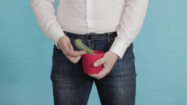 A man in a white shirt and jeans holds a red cactus pot against the background of his groin. The concept of erectile dysfunction in men, prostate disease, close-up