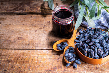 Small glass jar with homemade  haskap berry jam, on wooden background with bowl of fresh haskap...