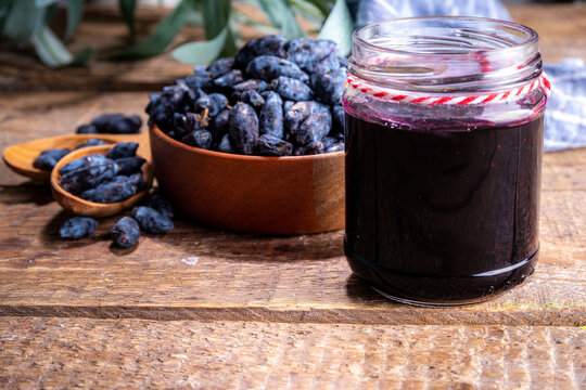 Small glass jar with homemade  haskap berry jam, on wooden background with bowl of fresh haskap (honeysuckle, honeyberry) berries, copy space